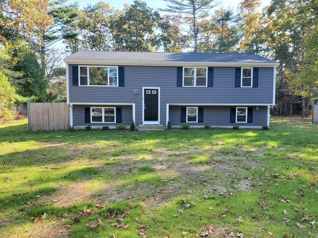 Split-level house with gray siding, black shutters, and a black front door, in a yard.