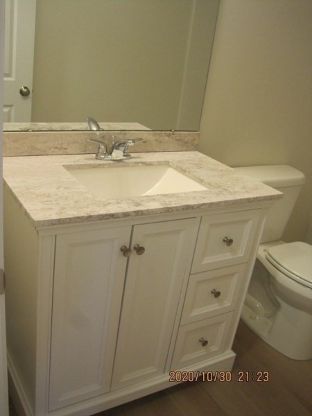 White bathroom vanity with sink, mirror, marble countertop, and toilet beside it.