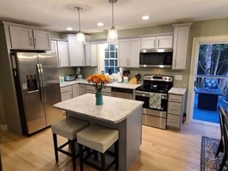 Modern kitchen with stainless steel appliances, island, and two stools under pendant lights.