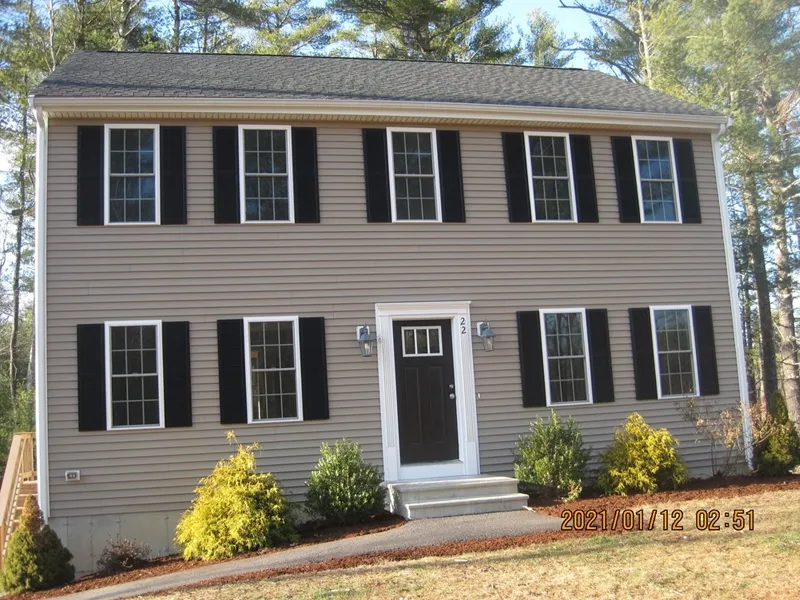Two-story beige house with black shutters, a black door, and small shrubs in front.