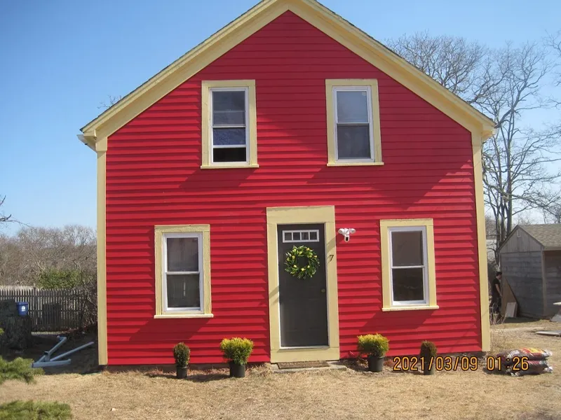 Bright red house with cream trim, black door, and five windows on a sunny day.
