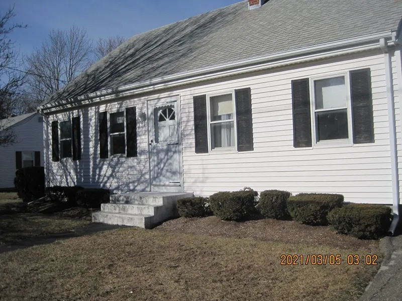 White house with black shutters, front steps, and trimmed bushes along the walkway.
