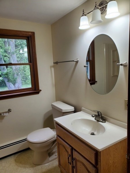 Bathroom with wood-trimmed window, toilet, sink, oval mirror, and wall lights.