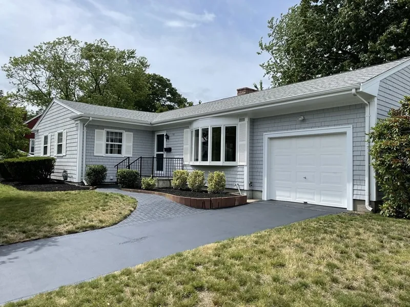 Single-story gray house with a bay window, attached garage, and a paved driveway.