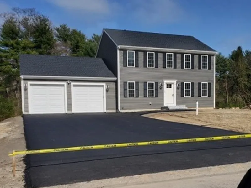 Newly paved driveway in front of a two-story house, blocked off with caution tape.