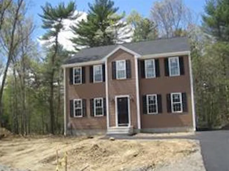 Two-story brown house with black shutters, surrounded by trees and a partly cleared yard.