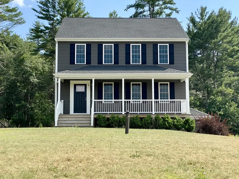 Two-story gray house with white trim, front porch, and a grassy lawn, surrounded by trees.
