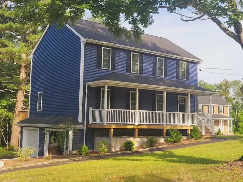 A blue two-story house with white trim, front porch, and attached garage on a grassy lawn.