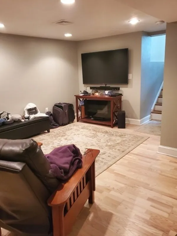 Basement room with TV, sofa, armchair, area rug, and stairs leading upward.