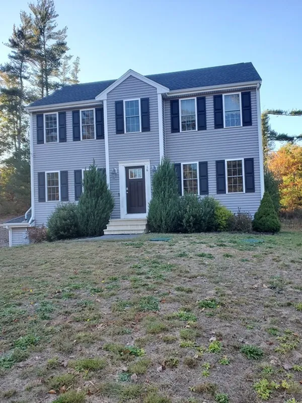 Two-story gray house with black shutters, white trim, and a front yard with sparse grass.