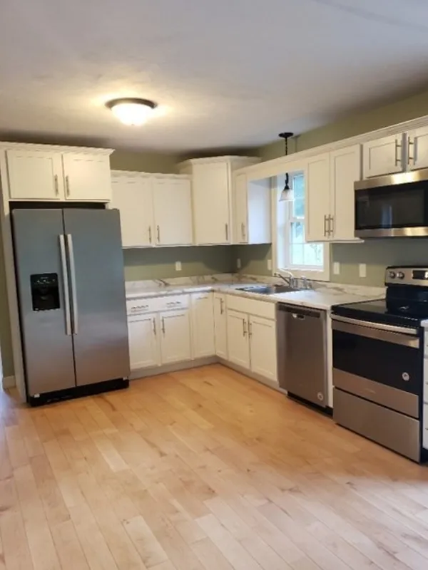 Modern kitchen with white cabinets, stainless steel appliances, and wood flooring.