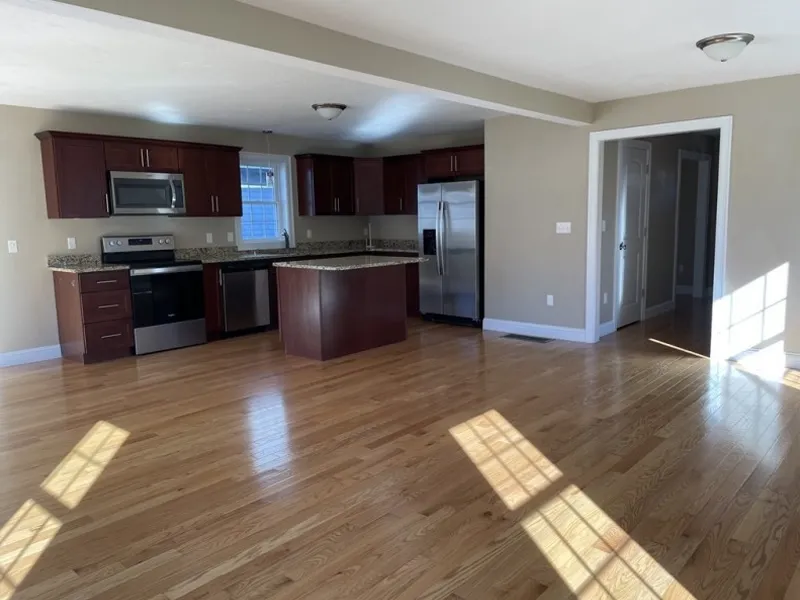 Open kitchen with wooden floors, dark cabinets, and stainless steel appliances, well-lit.