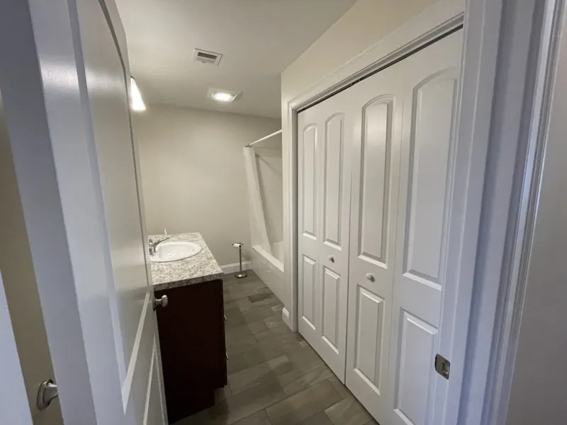 Modern bathroom with gray tile, white closet doors, vanity sink, and a shower in back.