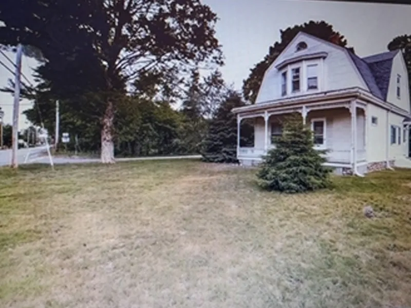 A white two-story house with a front porch, trees, and a grassy yard.