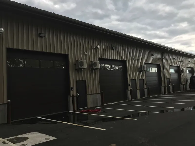 A row of closed garage doors on an industrial building with empty parking spaces.