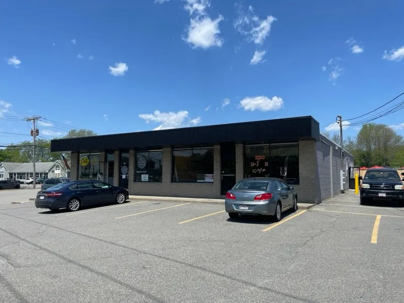Single-story commercial building with parked cars in front under a blue sky with clouds.