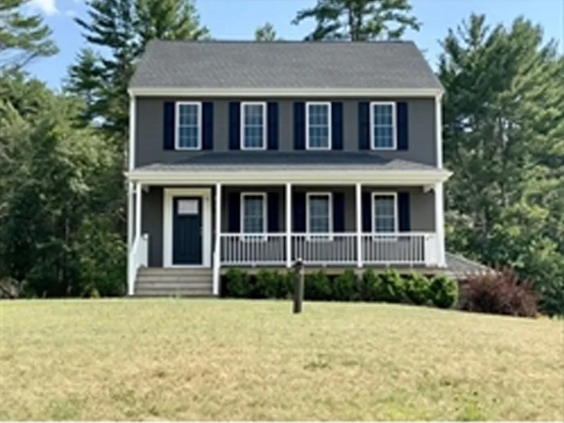 Two-story gray house with white trim, front porch, and shrubs, set on a grassy lawn.