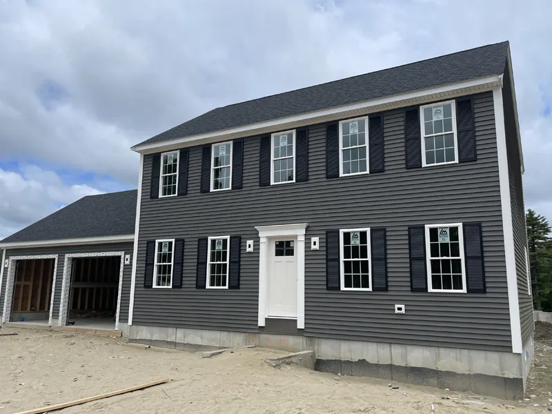 Two-story gray house with white trim, black shutters, and an attached garage under construction.