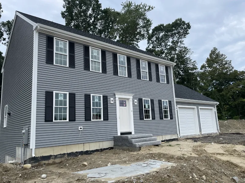 Gray two-story house with black shutters, white trim, and a two-car garage under cloudy sky.