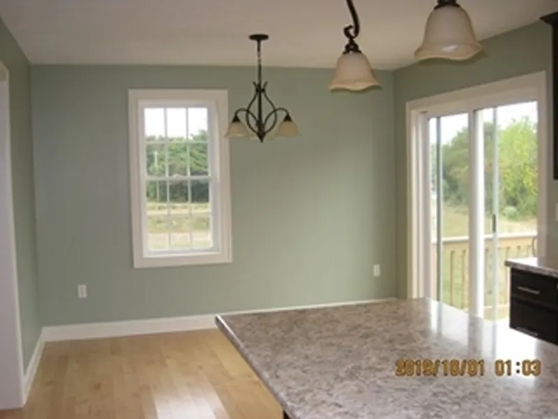 Bright kitchen with light green walls, marble counter, window, and glass sliding door.