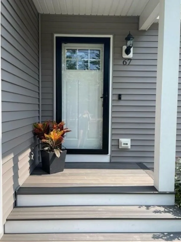 Gray front porch with a potted plant, glass door, and house number 67 on the siding.