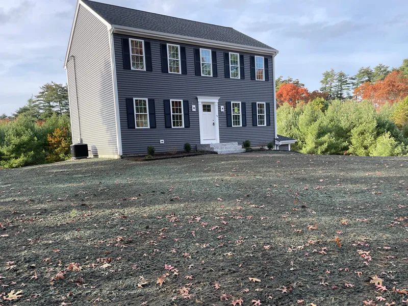 A two-story gray house with black shutters sits on a bare, newly seeded lawn.