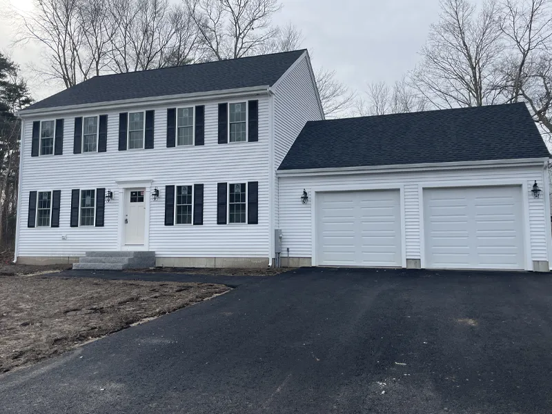 Two-story white house with black shutters and a double garage on a paved driveway.