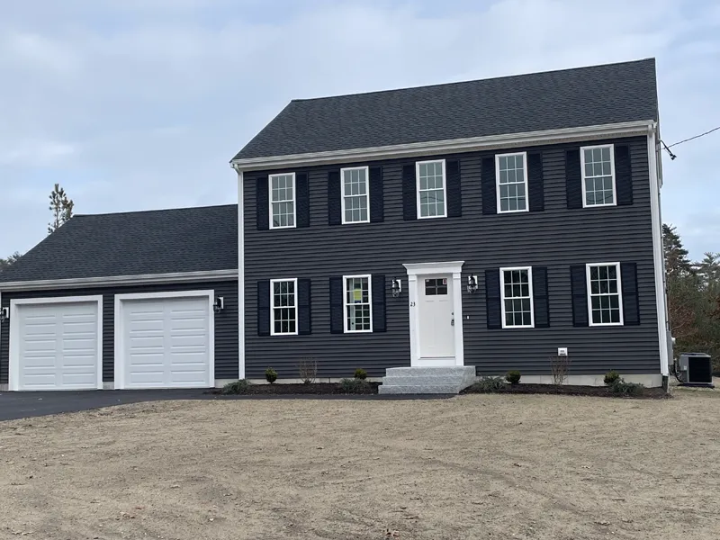 Two-story dark gray house with white trim and a double garage, on a barren yard.