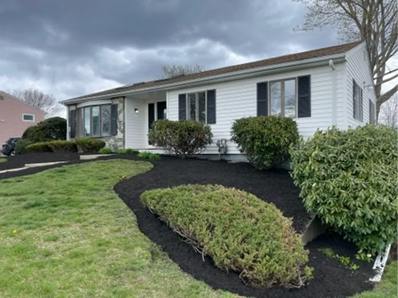 Single-story house with fresh black mulch and trimmed bushes under a cloudy sky.
