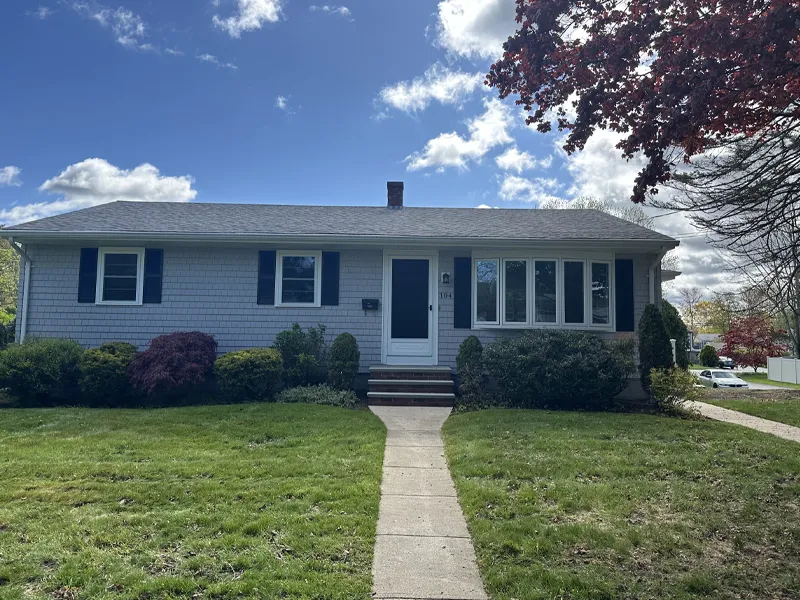 Single-story house with gray siding, blue shutters, and a front lawn under a blue sky.