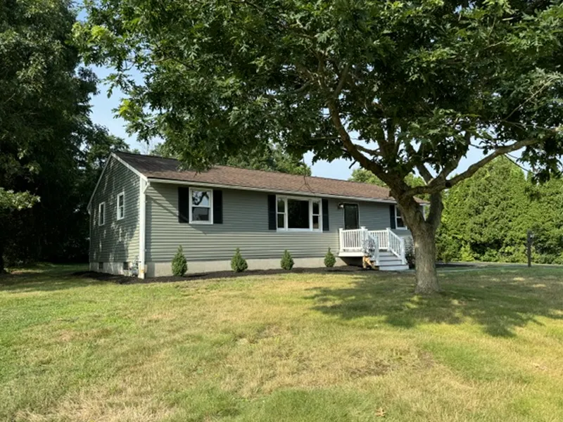 Single-story gray house with white trim, front steps, and a large tree in the yard.