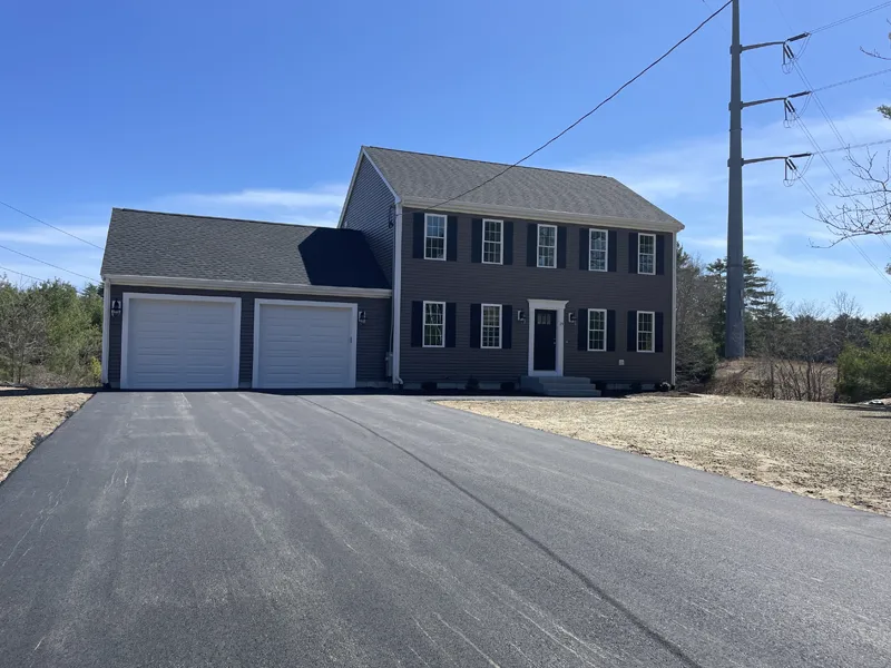 Two-story house with double garage and wide driveway under a clear blue sky.