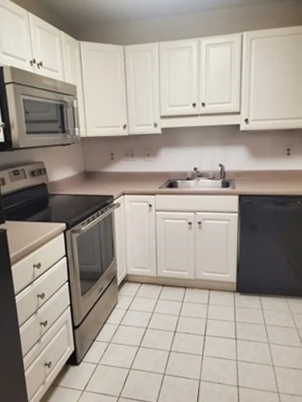 Modern kitchen with white cabinets, stainless steel appliances, and tiled floor.