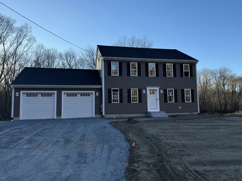Two-story house with attached double garage, gravel driveway, and bare yard, at dusk.