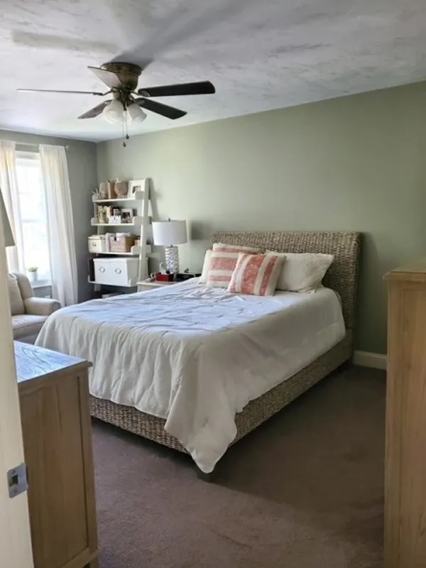 Cozy bedroom with a wicker bed, neutral bedding, and a shelf by the window.