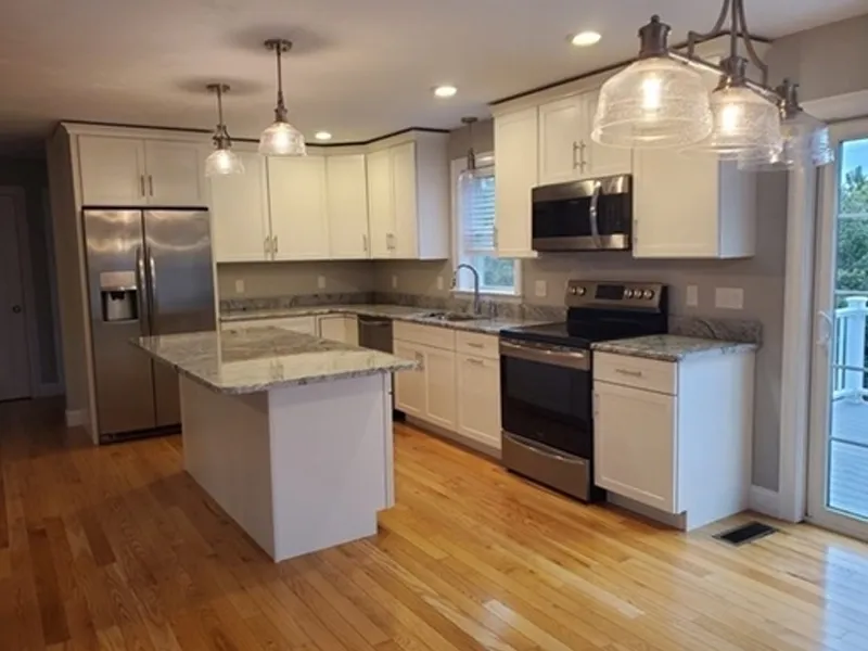 Modern kitchen with white cabinets, stainless steel appliances, and hardwood floors.