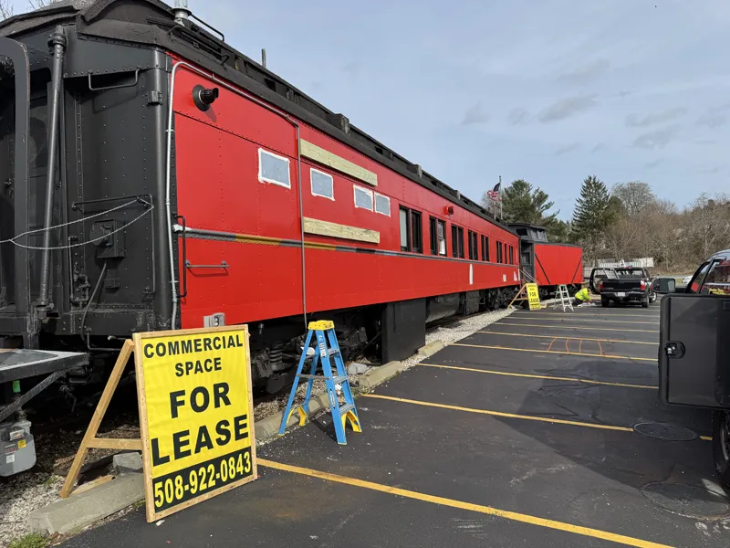 Red train car beside a parking lot with Commercial Space For Lease sign in front.