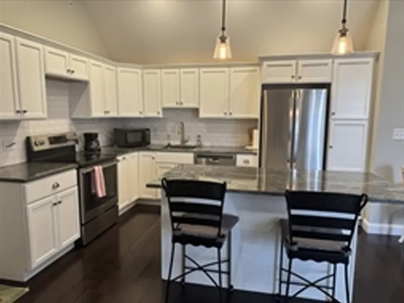 Modern kitchen with white cabinets, dark countertops, and two chairs at an island.