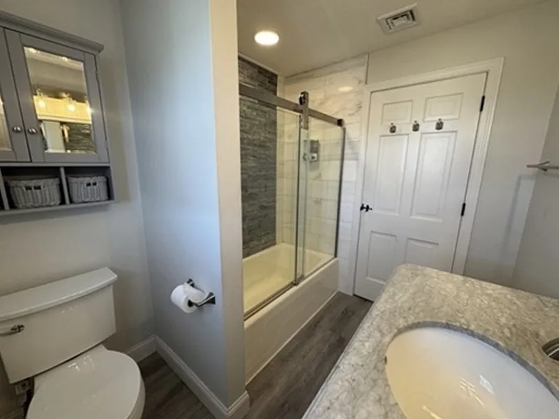 Modern bathroom with a glass shower, white toilet, and marble countertop sink.