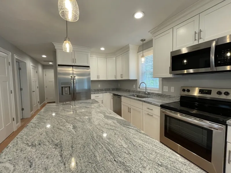 Modern kitchen with white cabinets, stainless steel appliances, and a granite island countertop.