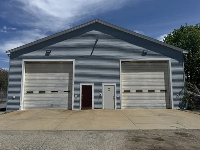 A gray industrial building with two large garage doors, a small door, and clear sky above.