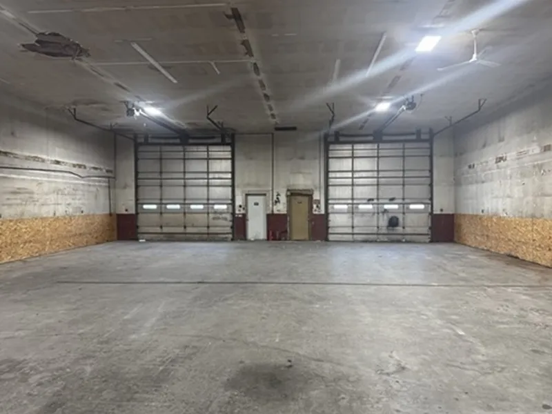 Empty industrial warehouse with two large garage doors and concrete floor.