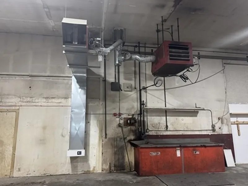 Industrial heating units and air ducts installed above a red metal workbench in a warehouse.