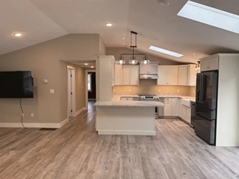 Modern kitchen with white cabinets, black appliances, and wood flooring under a vaulted ceiling.