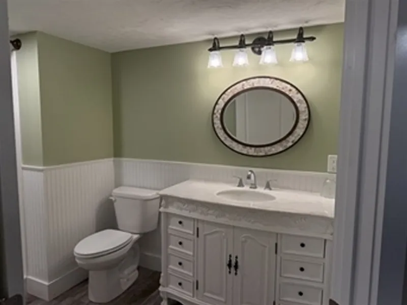 Bathroom with a white vanity, oval mirror, toilet, and four-bulb light fixture above.
