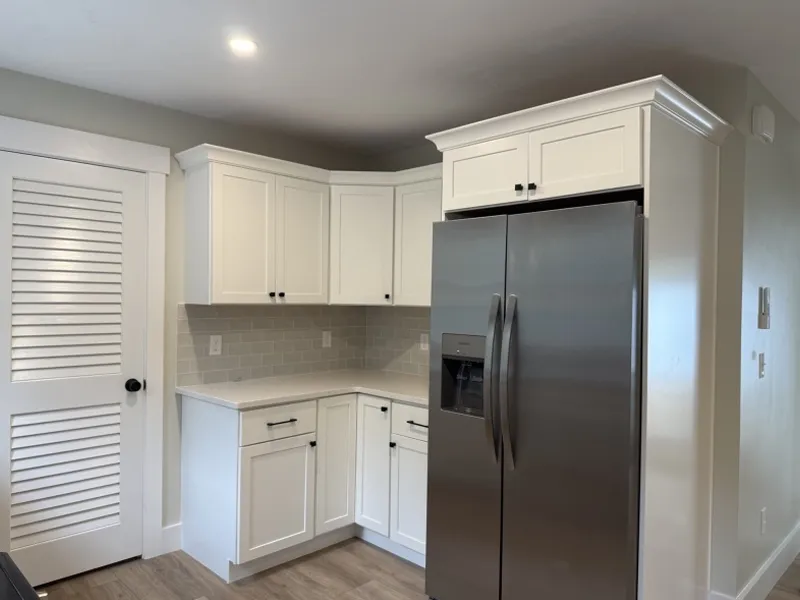 Modern kitchen with white cabinets, stainless steel fridge, and light wood flooring.