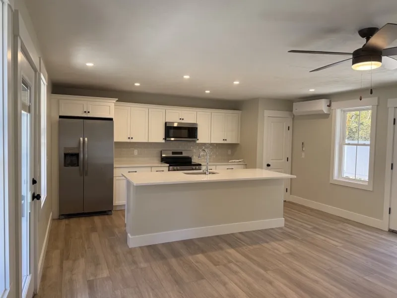 Modern kitchen with white cabinets, island, stainless appliances, and wood-style floor.