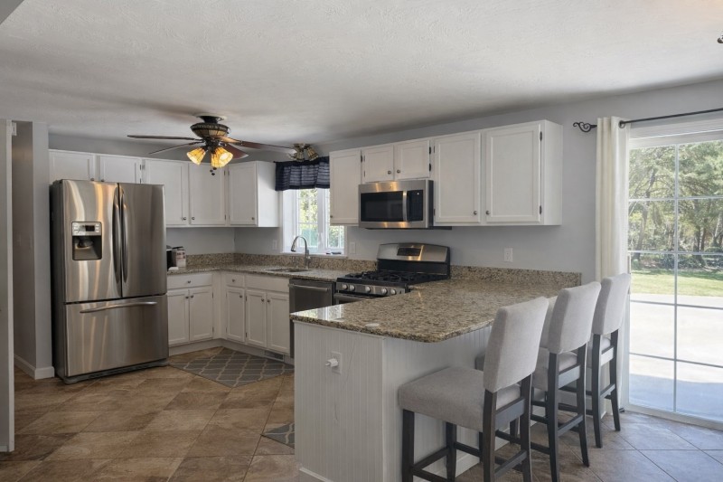 Modern kitchen with white cabinets, granite counters, and three bar stools by a glass door.