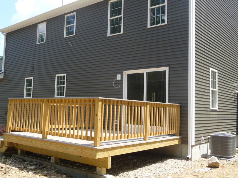 A newly built wooden deck attached to the back of a gray house with siding and windows.