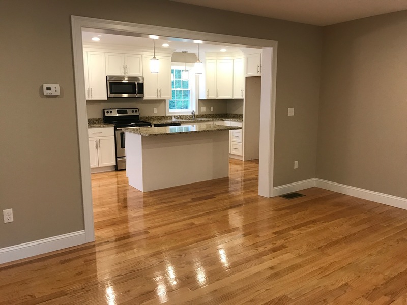 Modern kitchen with white cabinets, island, and stainless steel appliances, seen from living area.